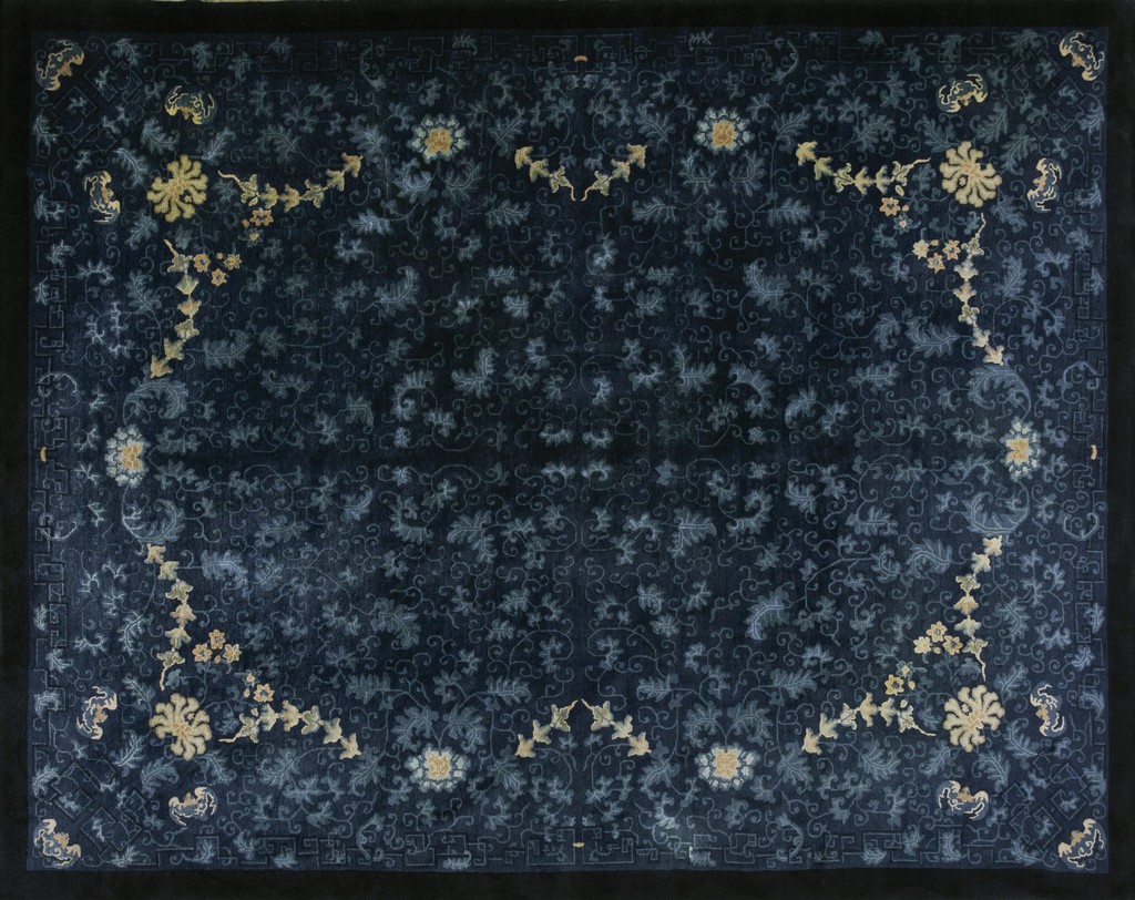 A rectangular antique chinese peking wool rug with a dark midnight blue field covered in light blue scrolling vines and accented by corner floral sprays in muted gold, bordered in solid black, by rugs on net.