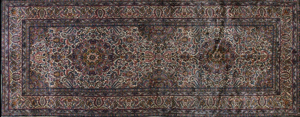 An overhead view of a rectangular antique persian-style rug featuring a dense, all-over pattern of intricate florals and paisley motifs in dark blues, reds, and cream colors, framed by a detailed border by rugs on net.
