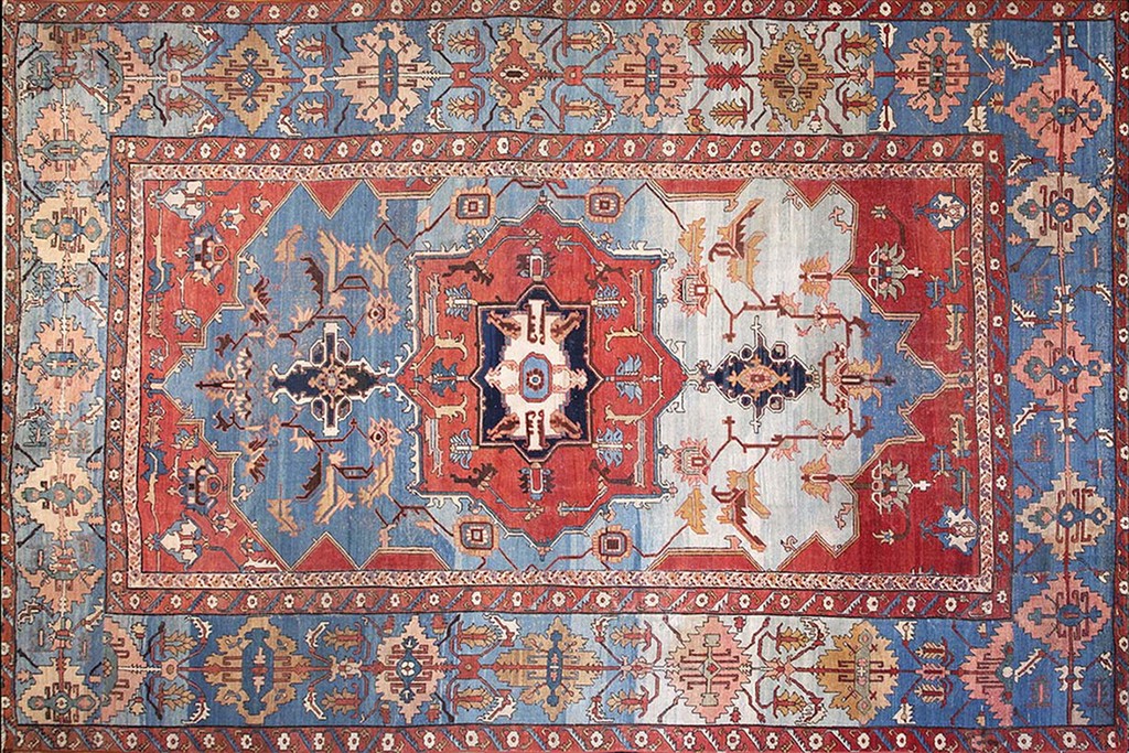 An overhead view of an antique serapi area rug featuring large geometric medallions in contrasting red and faded blue fields, framed by intricate borders. By rugs on net