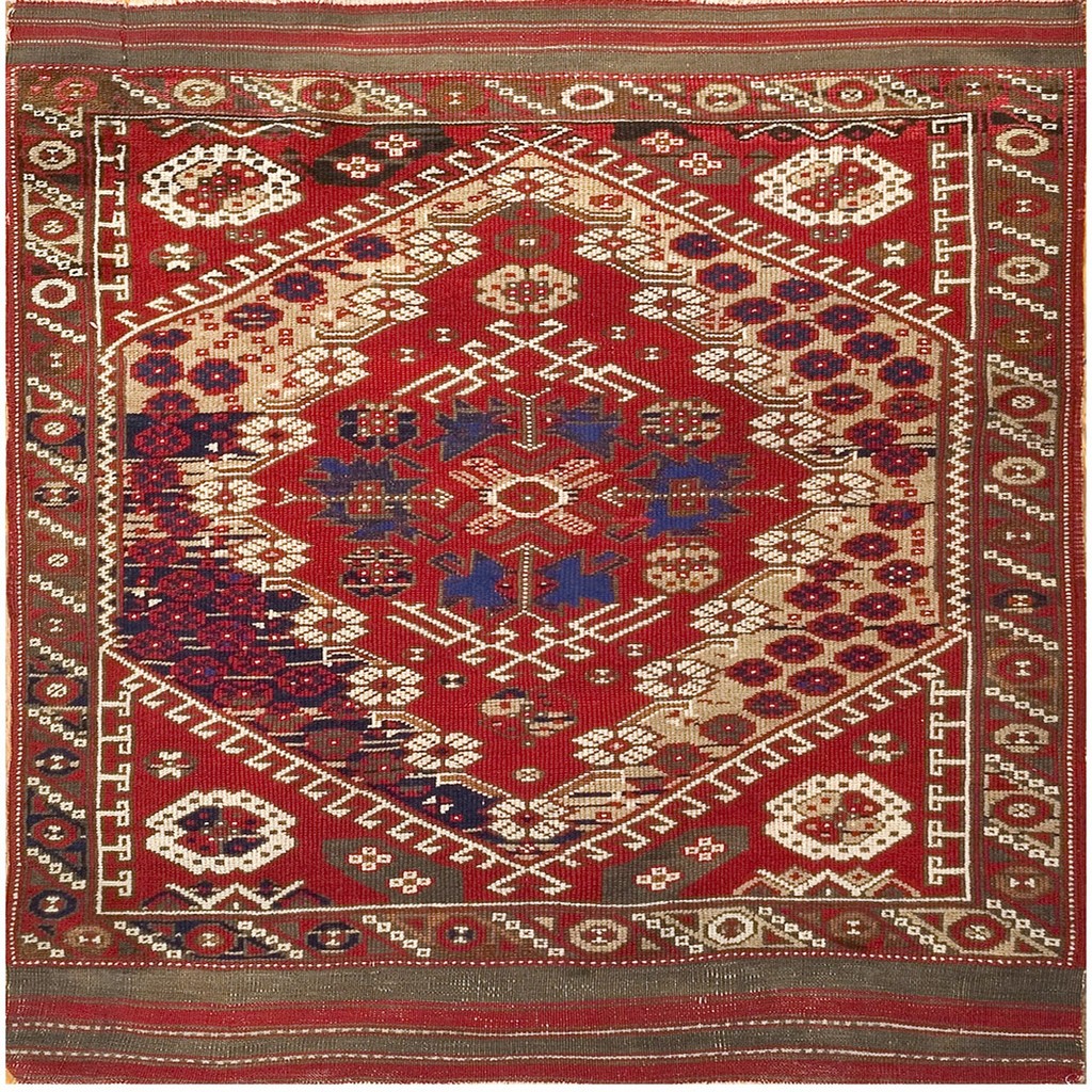 An antique turkish bergama knotted rug featuring a large central geometric medallion on a vibrant red field, accented with blue, beige, and white motifs. By rugs on net