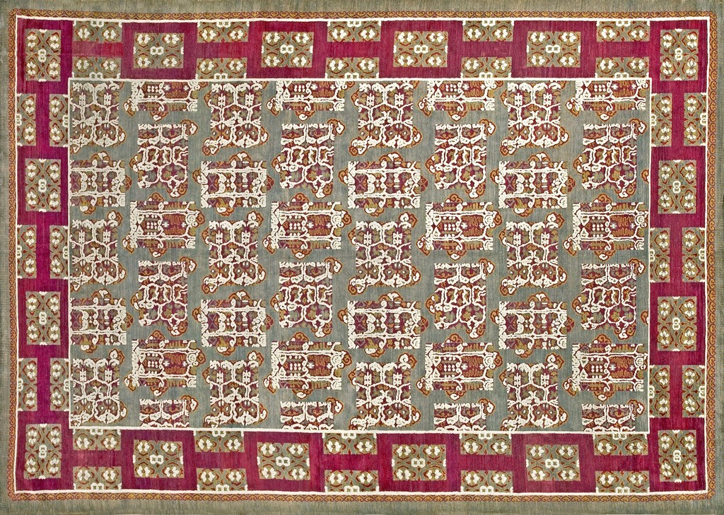 An antique knotted rug with gray rug colors featuring repeating stylized white and red geometric cartouches, framed by a wide magenta border with alternating patterned squares, by rugs on net.