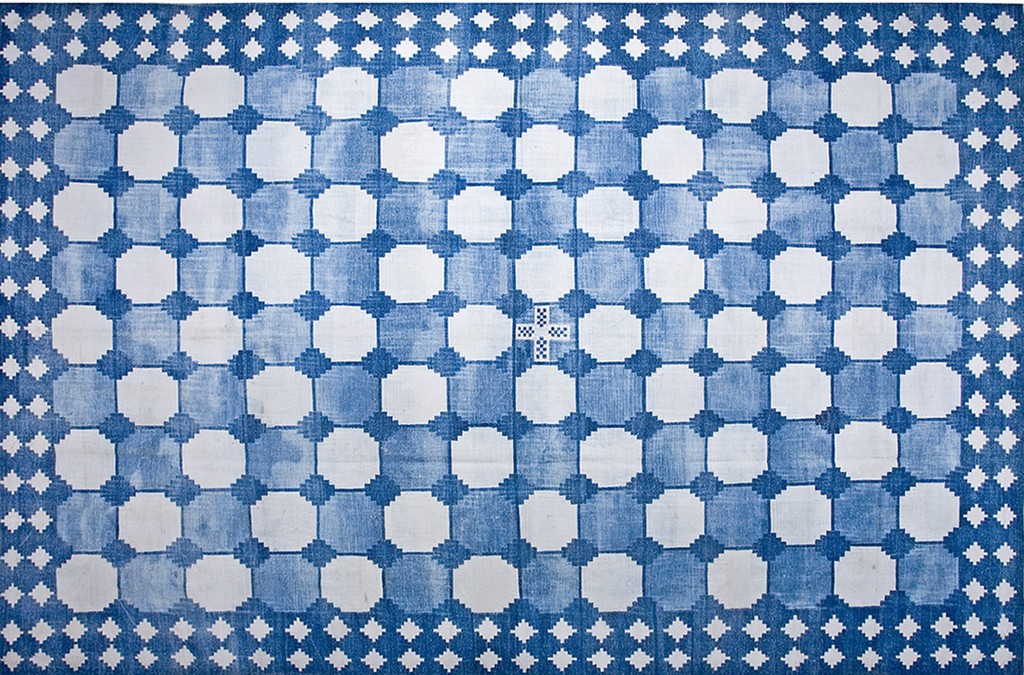 A flatweave rug with a repeating grid pattern of large white octagons alternating with blue squares, all surrounded by a blue border filled with small white diamond shapes, by rugs on net.