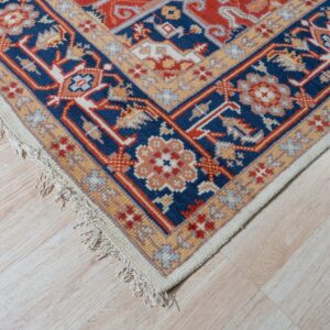 Corner view of a red and blue patterned rug on light flooring, placed between soft green and cream furniture.