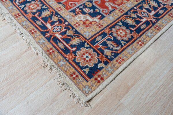 Corner view of a red and blue patterned rug on light flooring, placed between soft green and cream furniture.