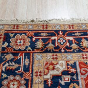 Ornate rug border in terracotta, navy, and ivory rests on light wood grain flooring.