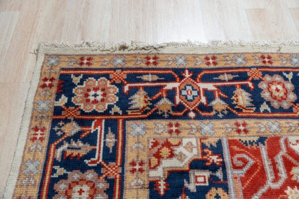 Ornate rug border in terracotta, navy, and ivory rests on light wood grain flooring.