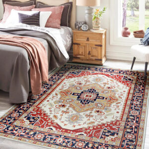 Red and ivory traditional area rug beneath a green velvet bedon light hardwood flooring.