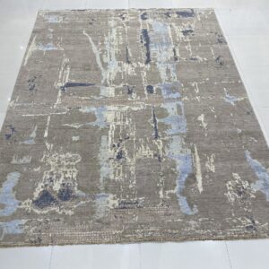 Abstract grey-brown rug with vertical patches of pale blue and dark blue displayed on white tile flooring.