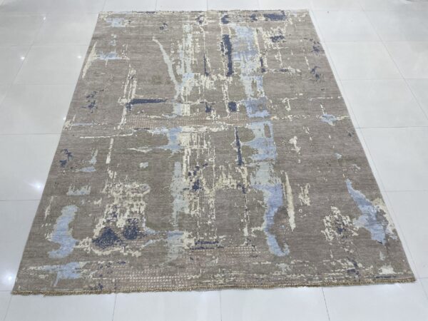 Abstract grey-brown rug with vertical patches of pale blue and dark blue displayed on white tile flooring.