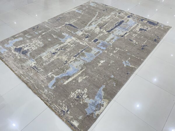 Abstract gray rug with blue and cream accents displayed on glossy white square tile.