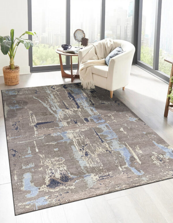 Abstract taupe rug with streaks of light and dark blue anchors a cream armchair by large windows.