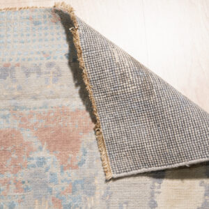 Abstract multicolored rug with blue and cream accents displayed on glossy white square tile.