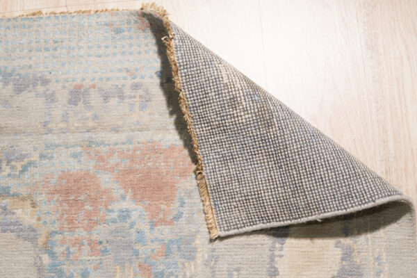 Abstract multicolored rug with blue and cream accents displayed on glossy white square tile.