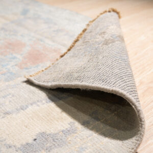 Abstract multicolored rug with blue and cream accents displayed on glossy white square tile.