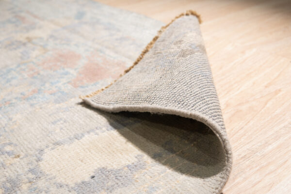 Abstract multicolored rug with blue and cream accents displayed on glossy white square tile.