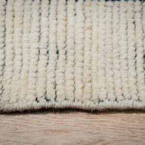 Creamy high-pile rug detail showing chunky texture and dark gray geometric stripes on light wood.