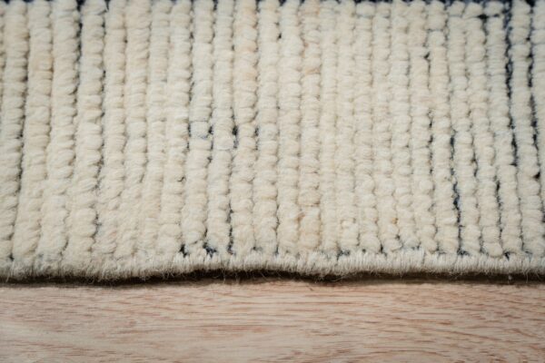 Creamy high-pile rug detail showing chunky texture and dark gray geometric stripes on light wood.