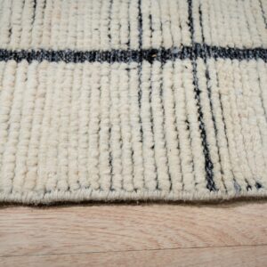 Edge of a thick, striped cream and dark gray rug lying on natural blonde wood flooring.