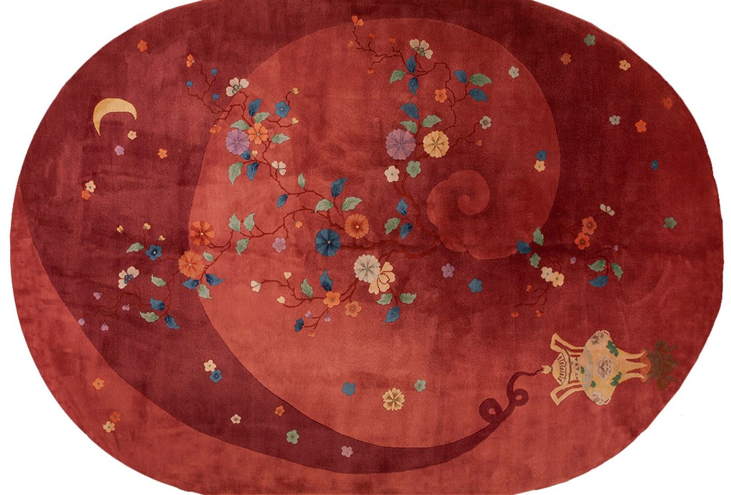 An oval antique chinese rug in deep rustic red, featuring a large, subtle spiral design that encompasses a flowing branch with colorful pastel flowers, a crescent moon, and a hanging lantern in the corner, by rugs on net