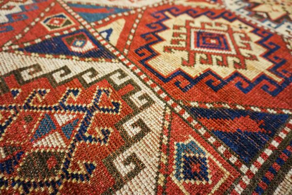 Close-up of geometric patterns in red, blue, and cream on a tribal rug by rugs on net. By rugs on net