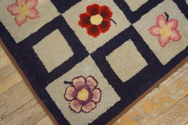 Close-up of a hooked rug with a navy blue grid pattern framing light squares, each containing a colorful flower, by rugs on net