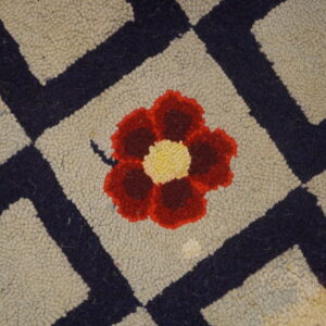 Close-up of a hooked rug featuring a central red and yellow flower within a beige diamond, bordered by dark blue lines, by Rugs On Net