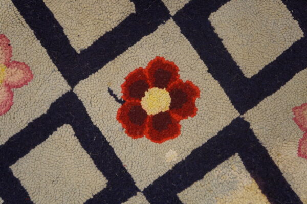 Close-up of a hooked rug featuring a central red and yellow flower within a beige diamond, bordered by dark blue lines, by rugs on net