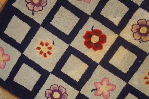 Close-up of a hooked rug featuring a light background, dark blue diamond lattice, and scattered colorful flowers, by rugs on net. By rugs on net