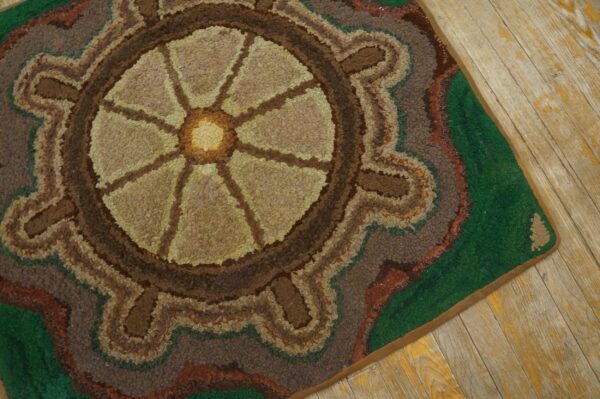 Close-up of a hooked rug featuring a circular, wheel-like design in earthy tones of brown and tan, set against a green border, by rugs on net. By rugs on net