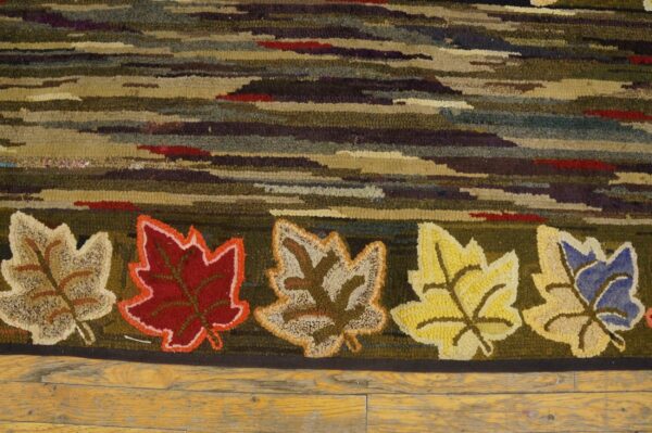 Close-up of a hooked rug featuring horizontal stripes and five distinct maple leaves in various colors, by rugs on net. By rugs on net