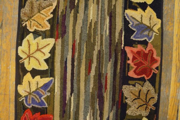 Close-up of a hooked rug featuring colorful autumn leaves against a striped, earthy-toned background, by rugs on net