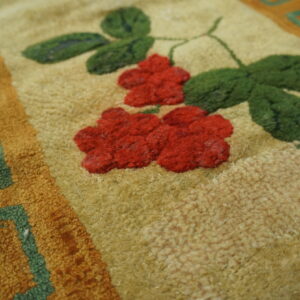 Close-up of a rug showing red flowers and green leaves on a tan background with a geometric border, by Rugs On Net