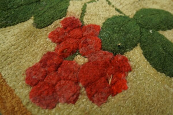 Close-up of a hooked rug featuring red floral elements on a tan background with green leaves, by rugs on net