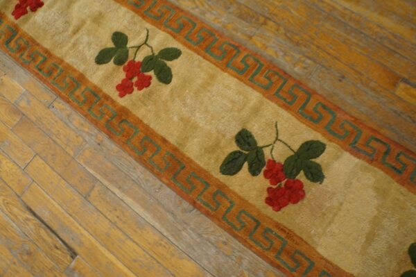 A close-up of the berry pattern rug showing red berries and green leaves on a tan field with a greek key border, by rugs on net. By rugs on net