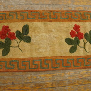 Close-up of a hooked rug featuring red floral clusters and green leaves on a tan field, bordered by an orange and green Greek key pattern, by Rugs On Net