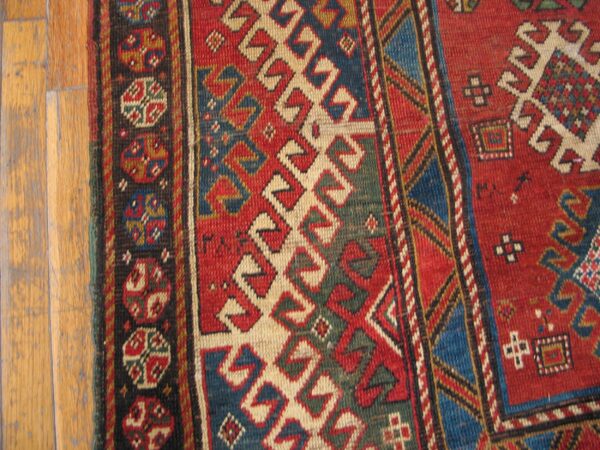 Close-up of a vibrant geometric pattern on a rug, featuring red, blue, and cream colors, next to wooden flooring, by rugs on net
