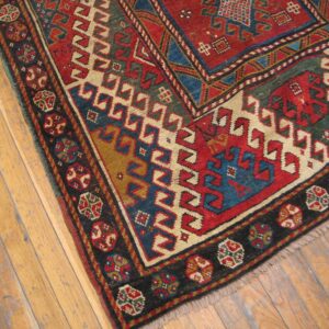 Close-up of a richly colored, geometric Caucasian rug corner on wooden floors by Rugs On Net. by Rugs On Net