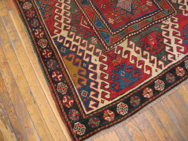 Close-up of a richly colored, geometric caucasian rug corner on wooden floors by rugs on net. By rugs on net