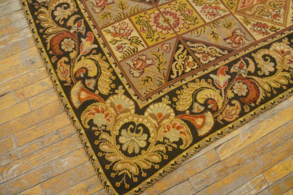 Close-up of a richly patterned, dark-bordered needlepoint rug on a worn wooden floor by rugs on net. By rugs on net