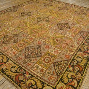 A large, antique-style rug featuring a geometric pattern of tiled diamonds in muted yellows, reds, and grays, framed by a dark border with large paisley motifs. This is the 'Antique Geometric Patchwork Rug' by Rugs On Net. by Rugs On Net