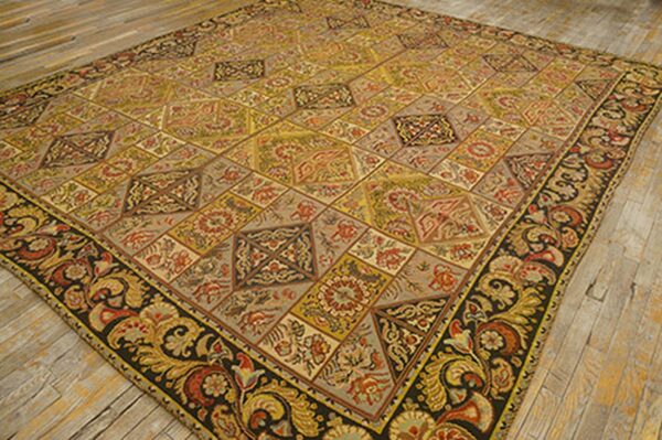 A large, antique-style rug featuring a geometric pattern of tiled diamonds in muted yellows, reds, and grays, framed by a dark border with large paisley motifs. This is the 'antique geometric patchwork rug' by rugs on net. By rugs on net
