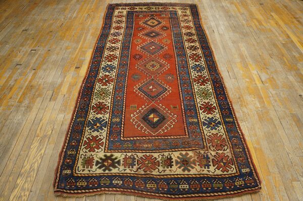A long runner rug with a dominant red field and geometric diamond motifs, bordered in blue and cream, displayed on a distressed wooden floor by rugs on net. By rugs on net