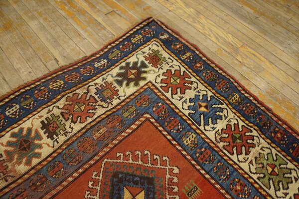Close-up corner of an antique rug with geometric patterns in red, blue, and cream, resting on distressed wood floors by rugs on net