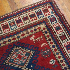 Close-up of a richly colored rug with geometric patterns in red, blue, and cream on a wooden floor by Rugs On Net