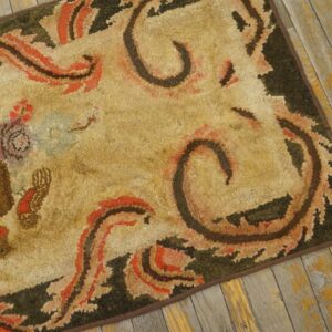 Close-up of a vintage hooked rug with beige, orange, and dark green patterns on a distressed wooden floor, by Rugs On Net