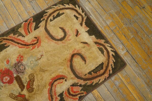 Close-up of a hooked rug with beige, brown, and red floral/scroll motifs on a dark border, resting on distressed yellow wood flooring by rugs on net