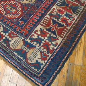 Close-up corner detail of a vintage rug with geometric patterns in red, blue, and cream on a wooden floor, by Rugs On Net