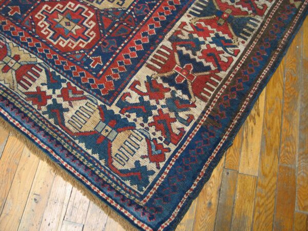Close-up corner detail of a vintage rug with geometric patterns in red, blue, and cream on a wooden floor, by rugs on net