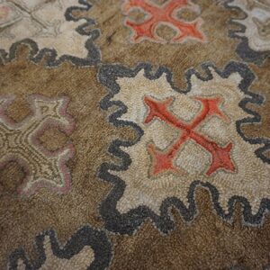Close-up of a brown rug featuring repeating stylized cross motifs in red and beige with dark outlines by Rugs On Net