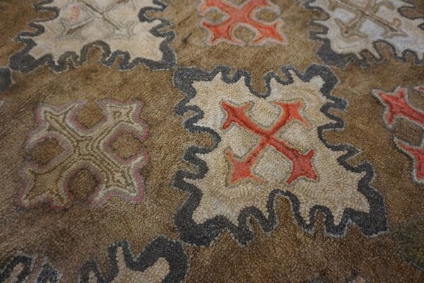 Close-up of a brown rug featuring repeating stylized cross motifs in red and beige with dark outlines by rugs on net